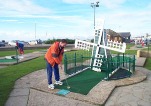 Photo of John Moore playing a shot at the crazy golf hole with the windmill.