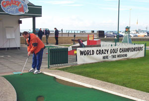 Photo of John Moore on first hole at Hastings Crazy Golf. Banner advertising the World Championship is displayed nearby.